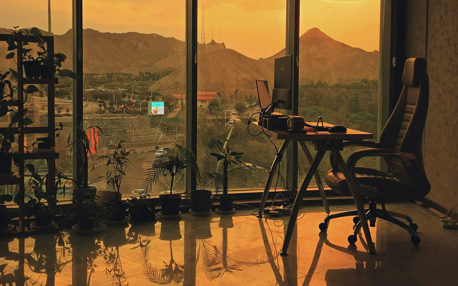 Desk and chair beside floor-to-ceiling windows overlooking mountains at sunset