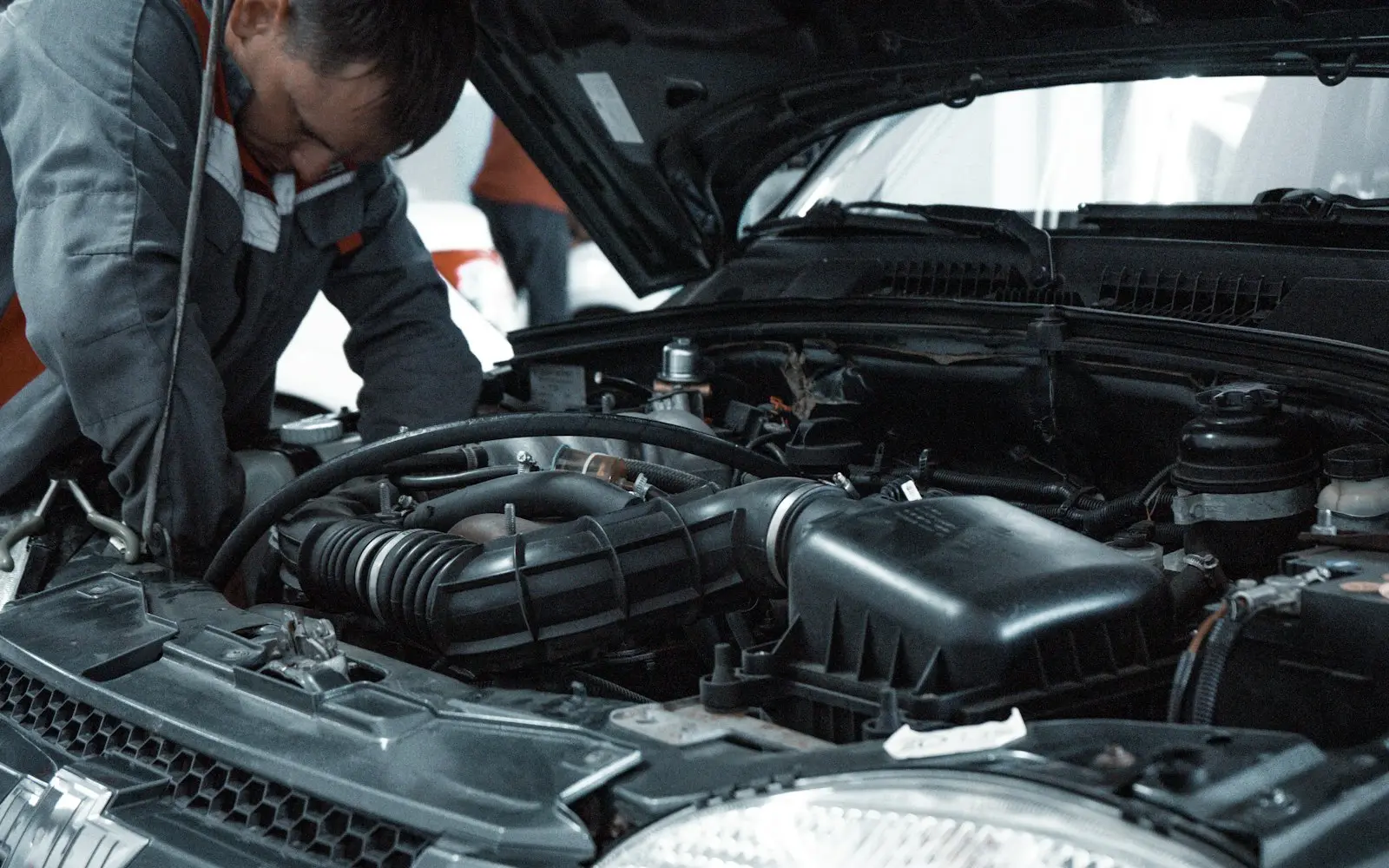Mechanic in a grey uniform inspecting a car engine in a workshop