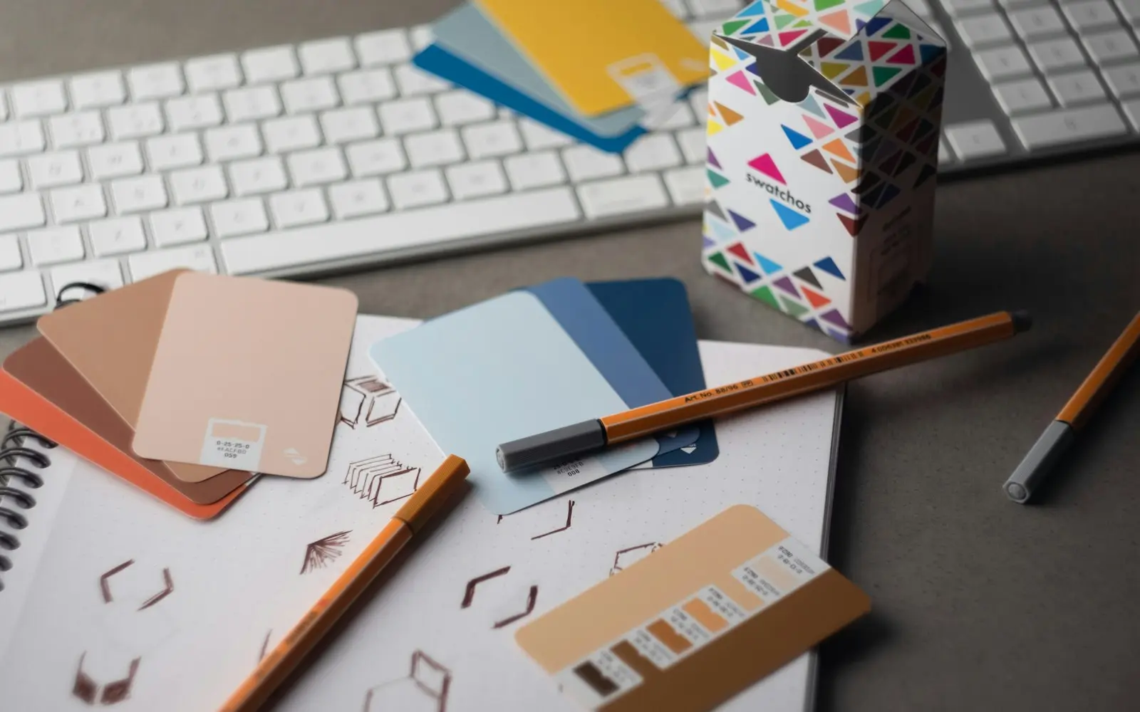 Colour sample cards, pencils and logo sketches on a desk beside a keyboard