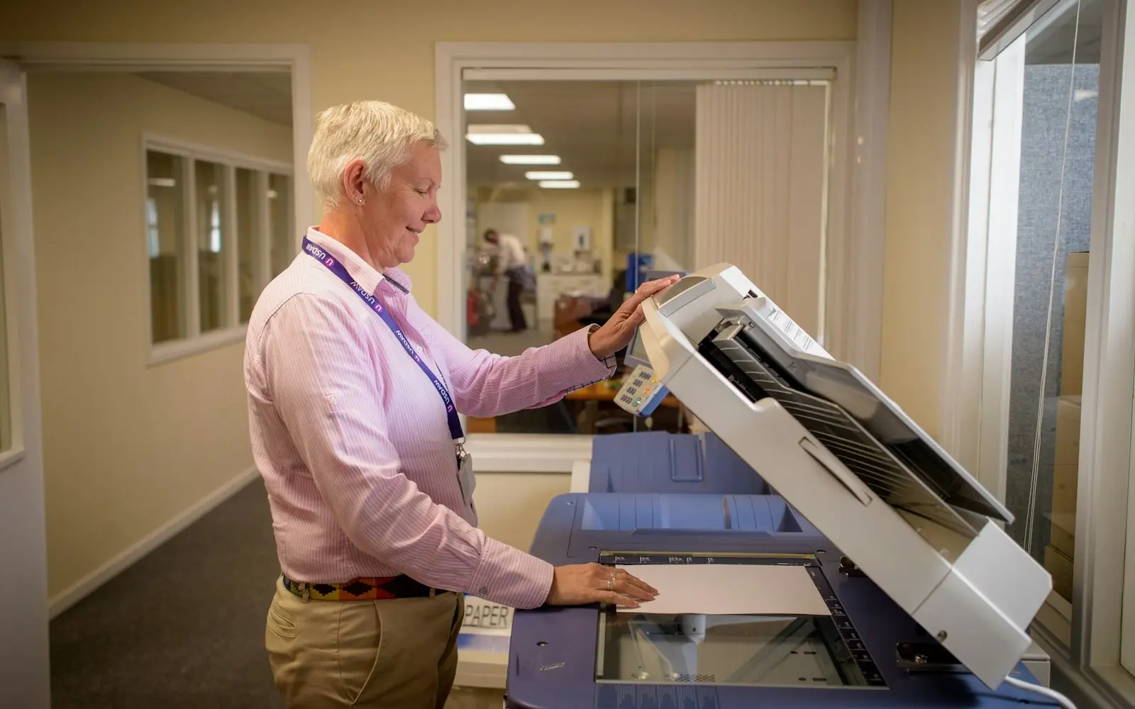 Office worker placing paperwork on a document scanner in a bright corridor