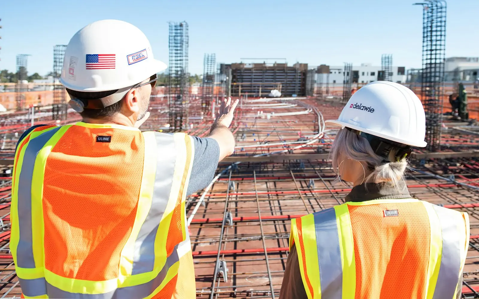 Two engineers in hard hats and safety vests looking over a construction site