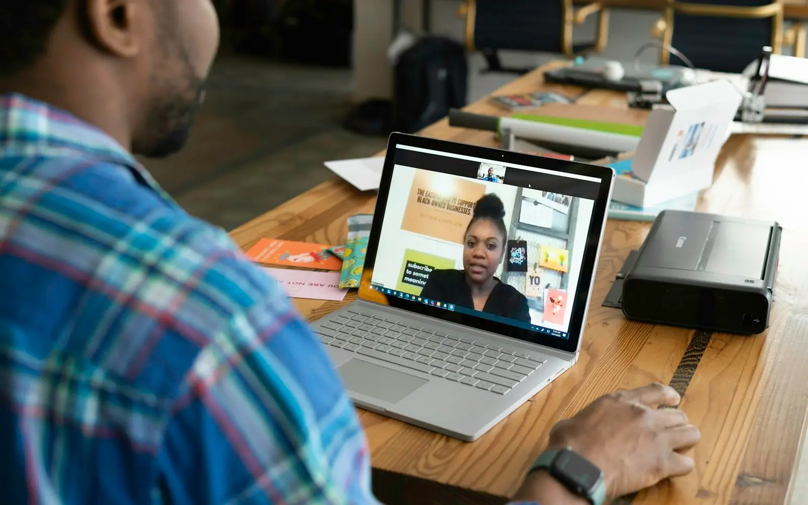 Man on a video call with a woman shown on a laptop screen at a wooden desk