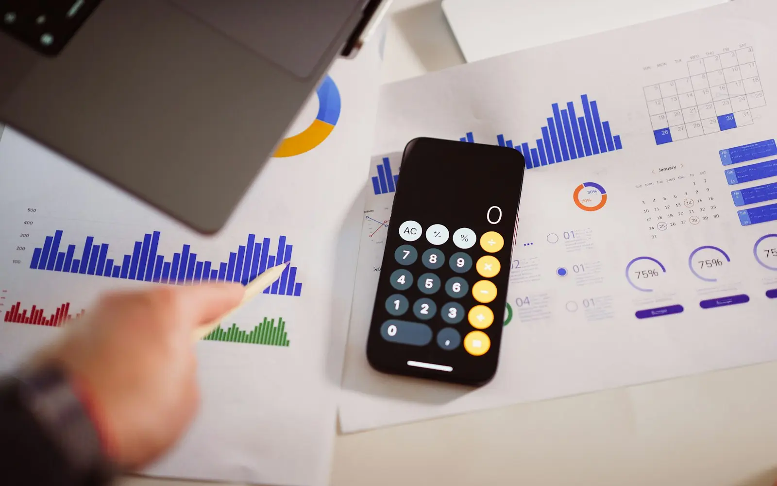 Printed charts and a phone calculator on a desk beside a laptop