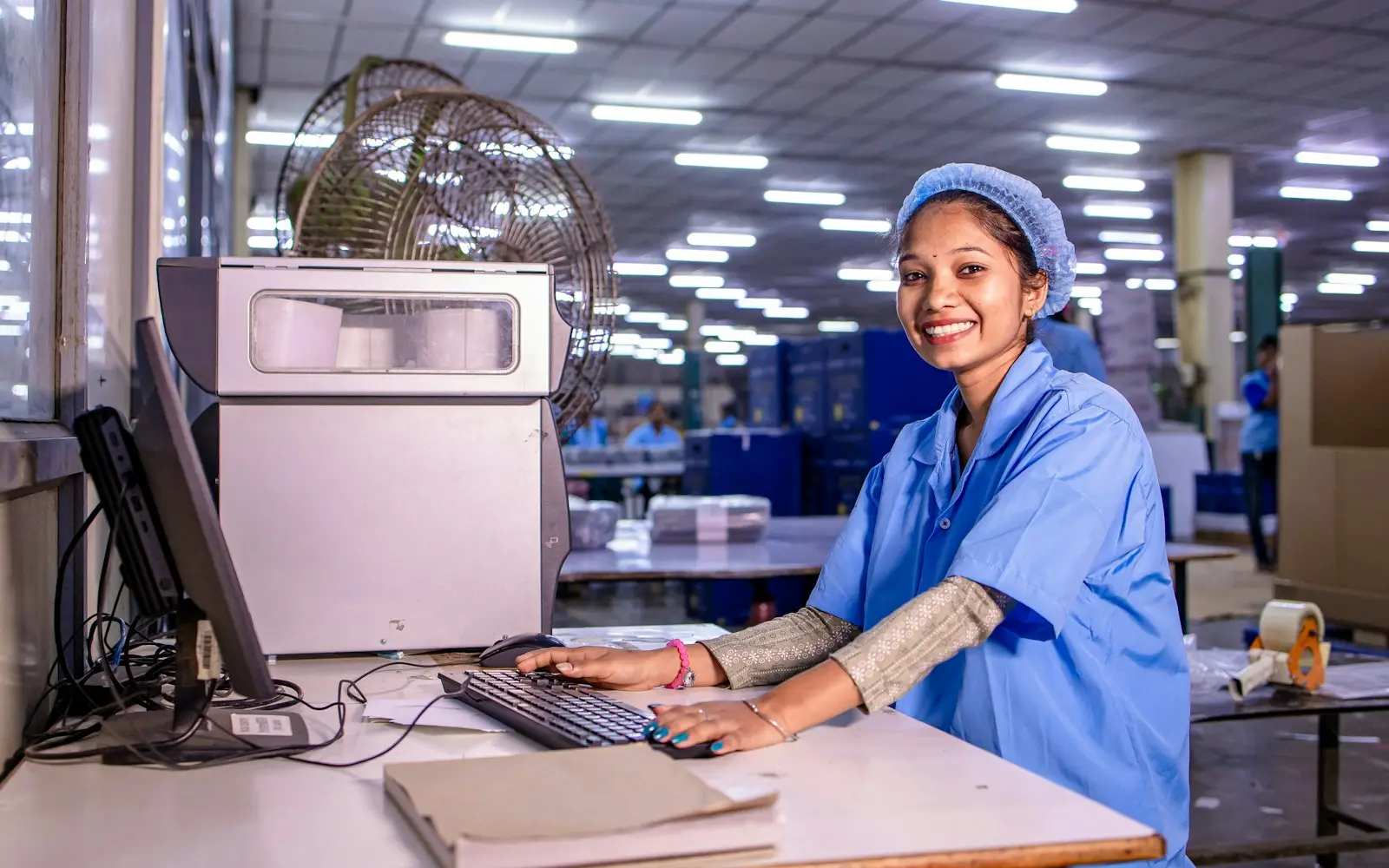 Smiling factory worker at a computer workstation on a production floor