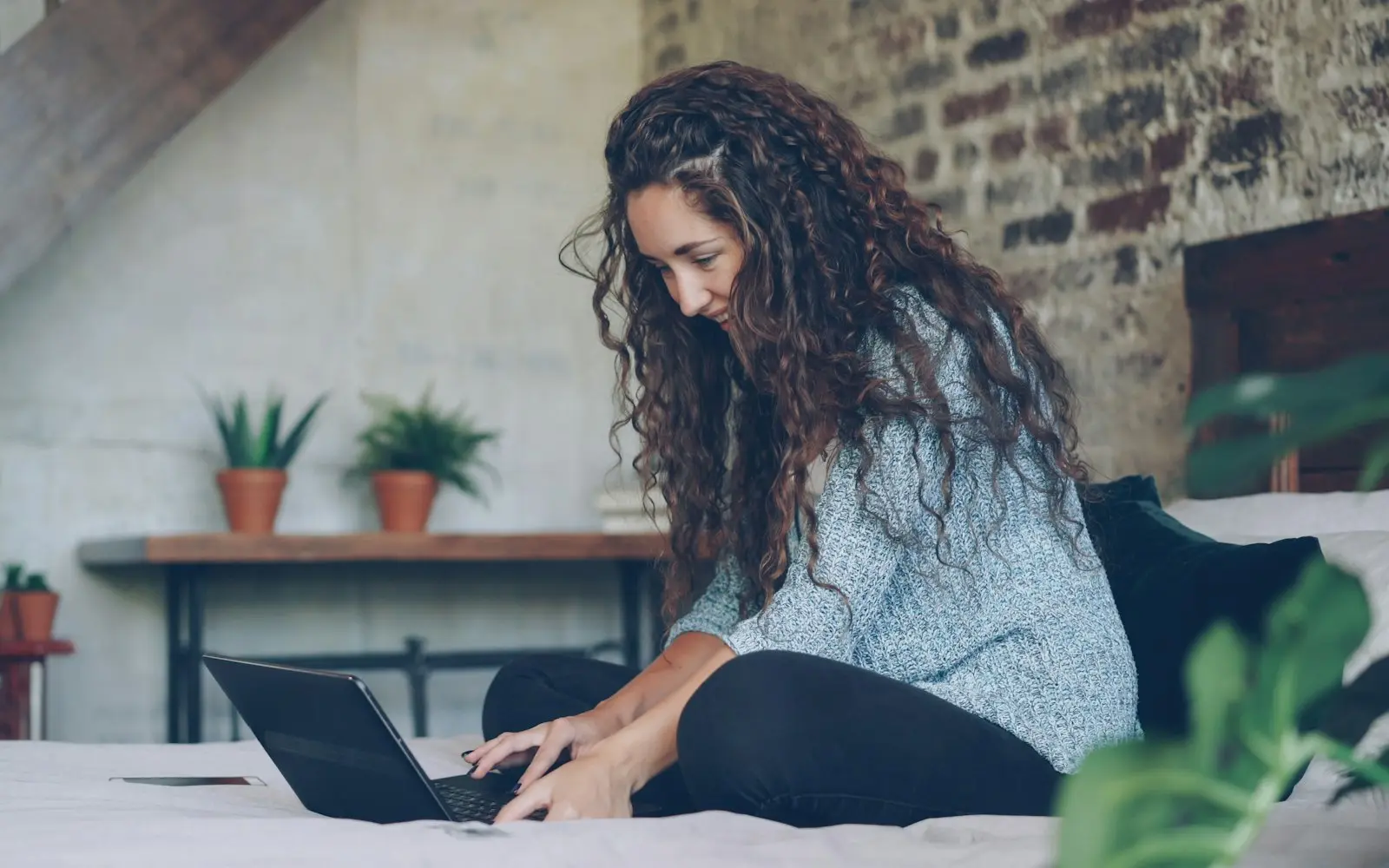 Woman with curly hair typing on a laptop in a bright loft