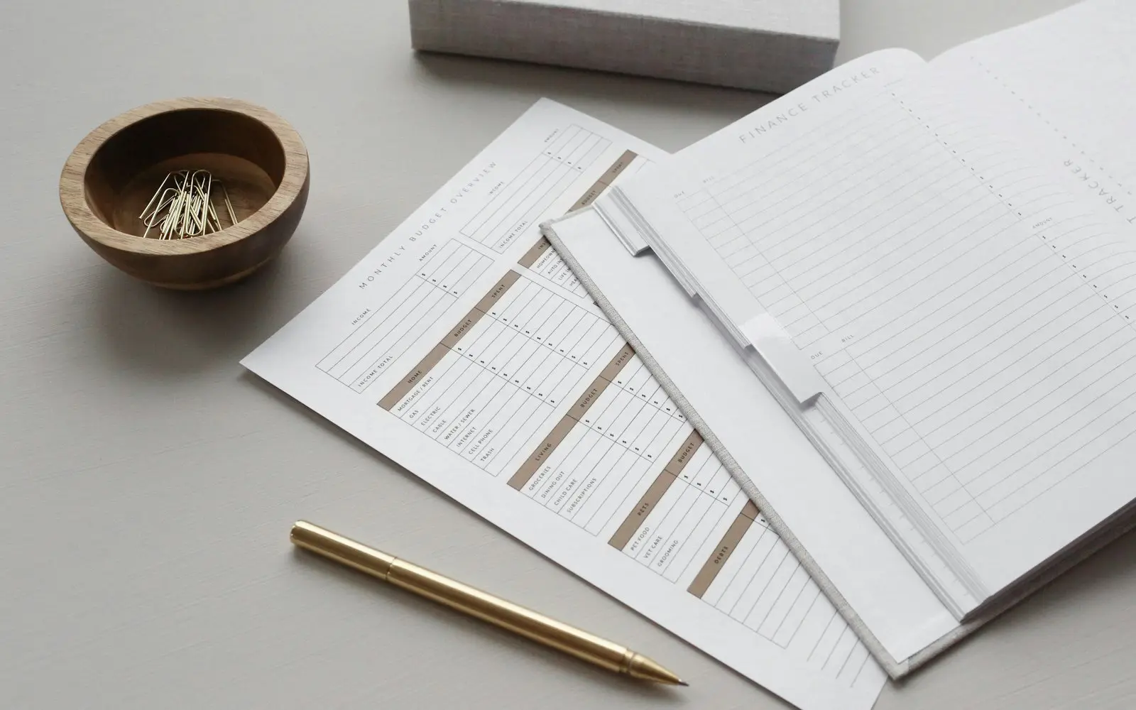 Printed budget sheets and a notebook with a gold pen on a pale desk