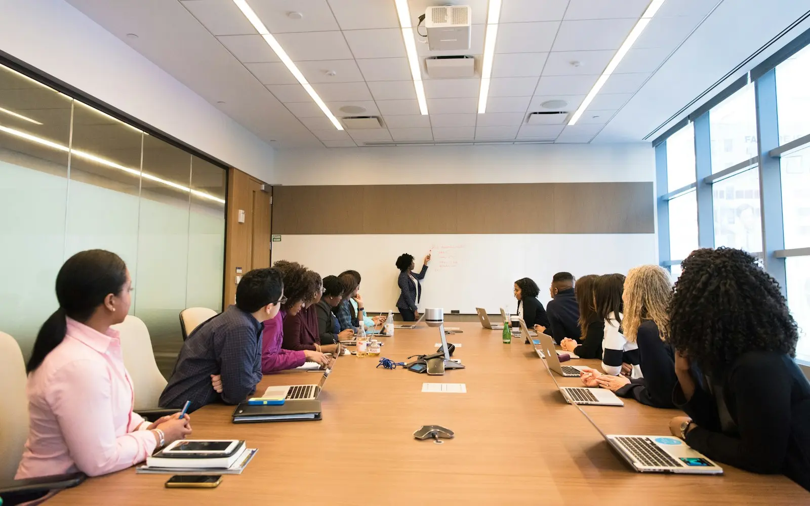 Colleagues with laptops listening to a presenter at a long boardroom table