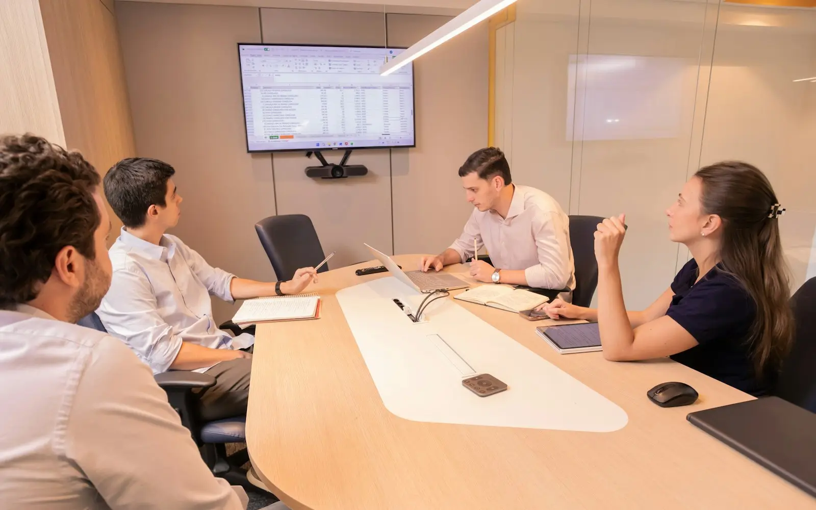 Colleagues around an oval meeting table looking at a spreadsheet on a wall screen