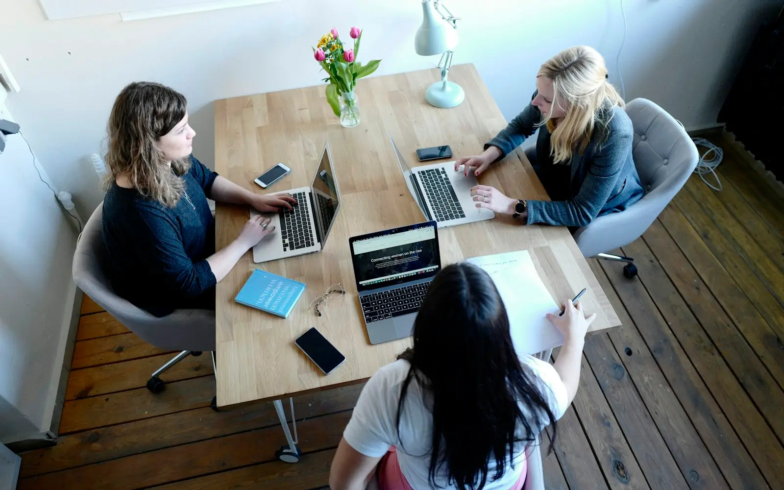 Overhead view of four colleagues with laptops and notebooks around a wooden table