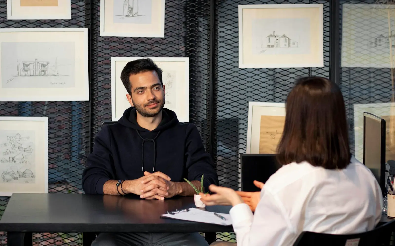 Two people in conversation across a dark desk in a design studio