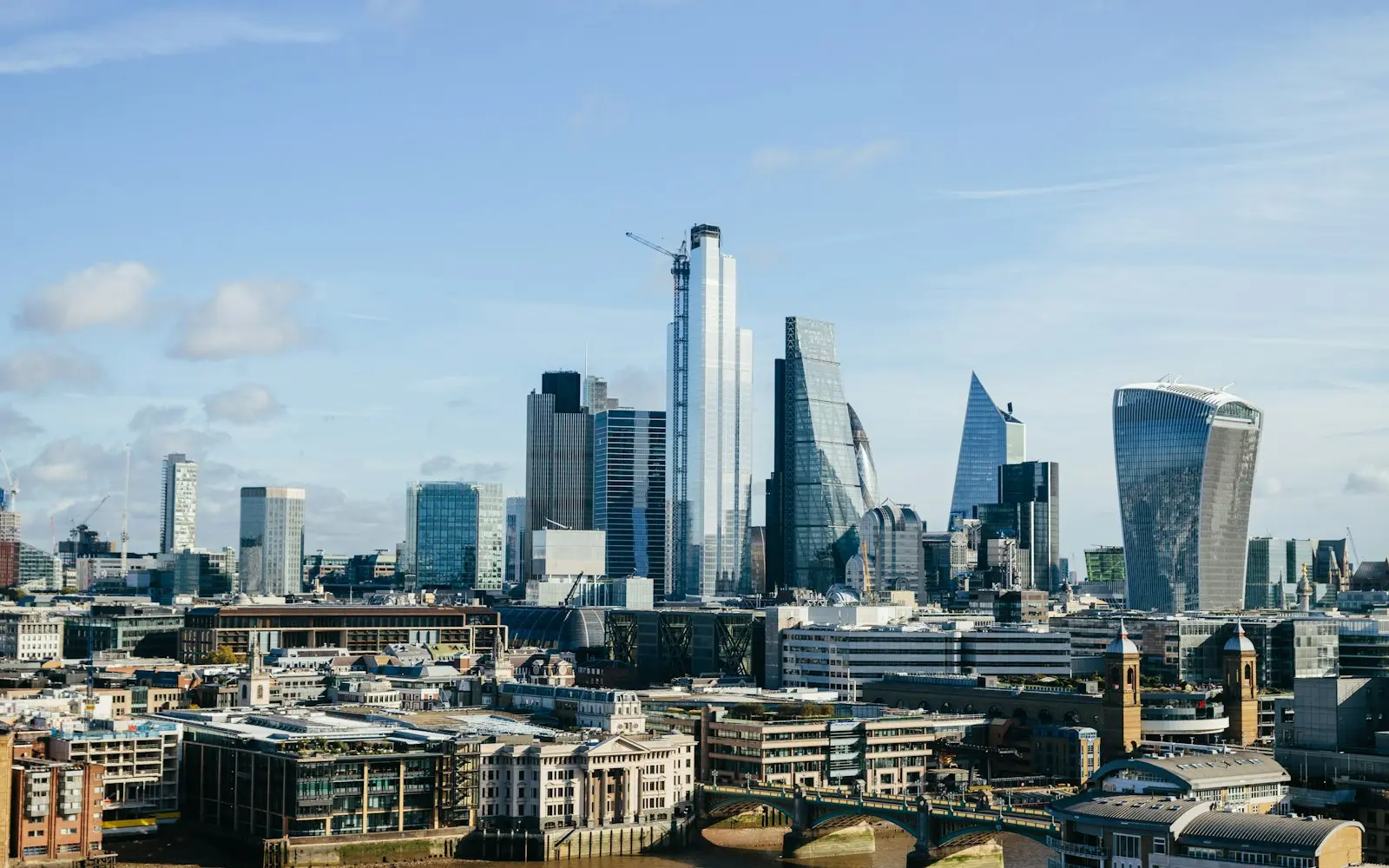 City skyline of glass office towers under a blue sky with scattered clouds