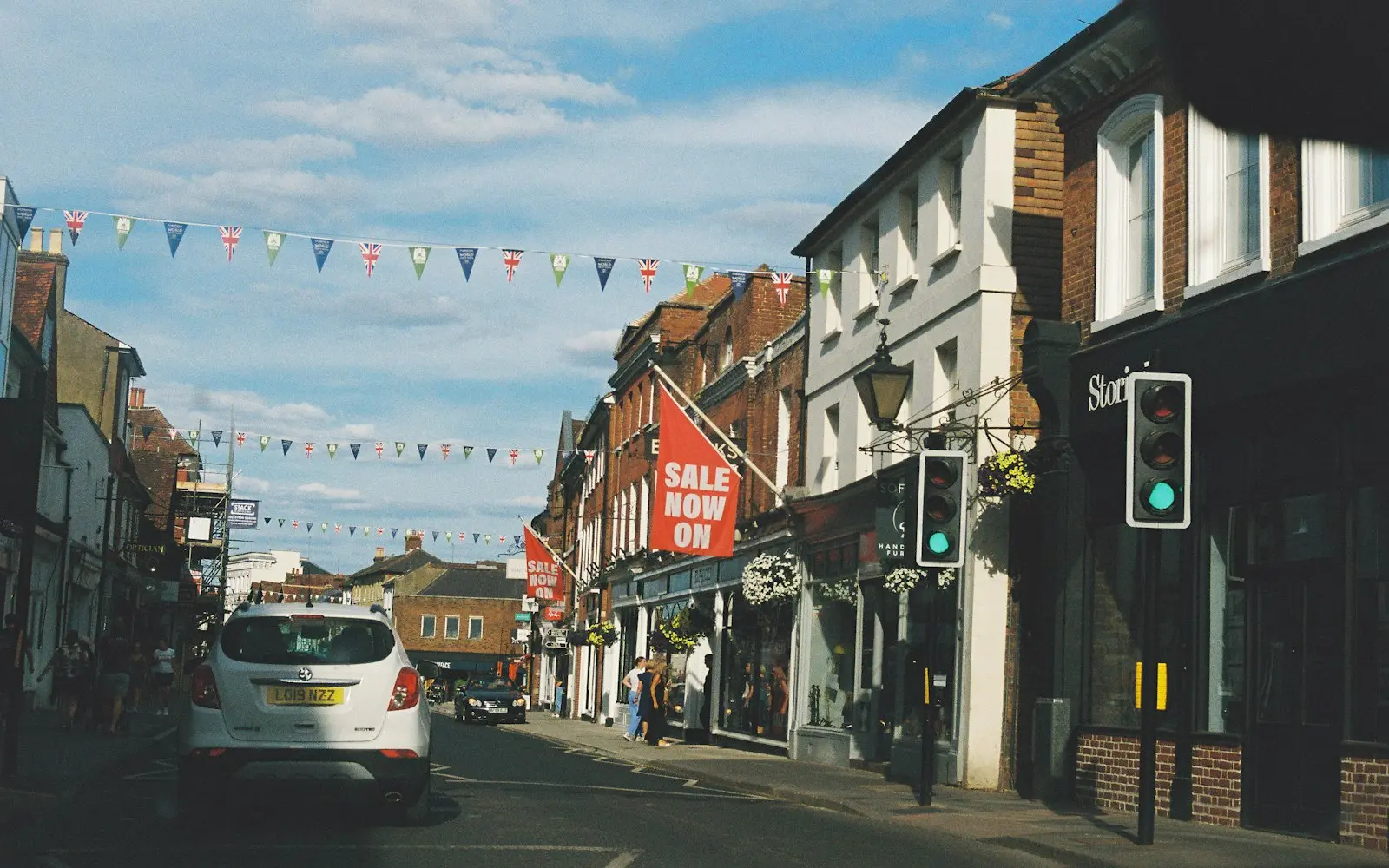 Bunting strung over a busy high street lined with small shops under a blue sky