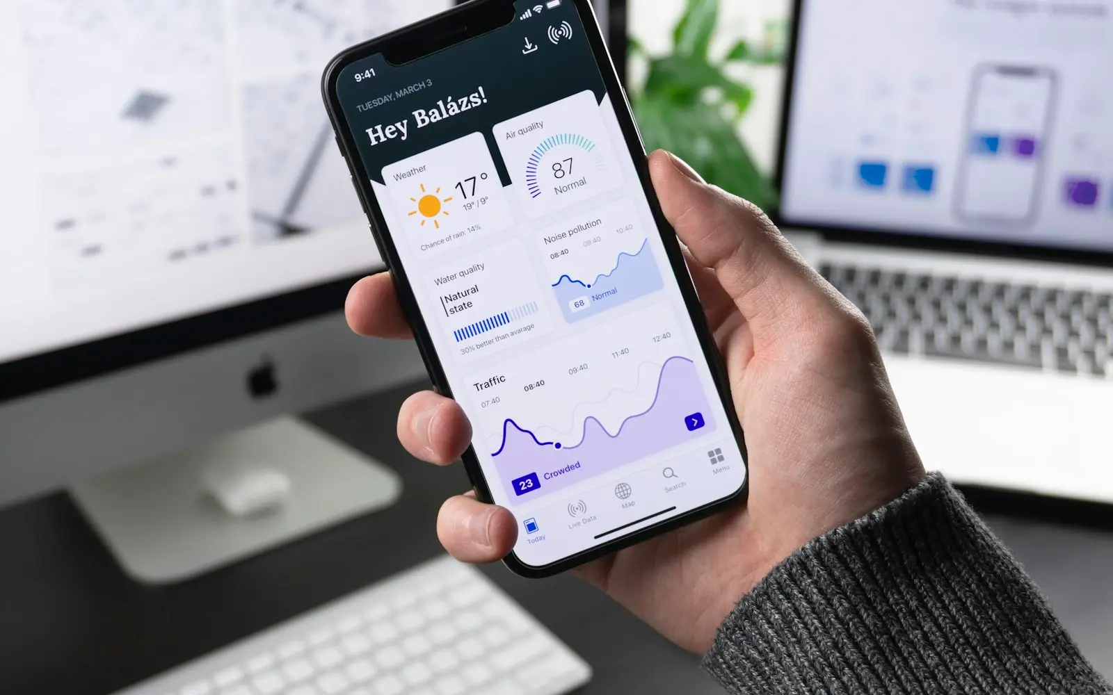 Hand holding a smartphone showing an app dashboard beside interface sketches