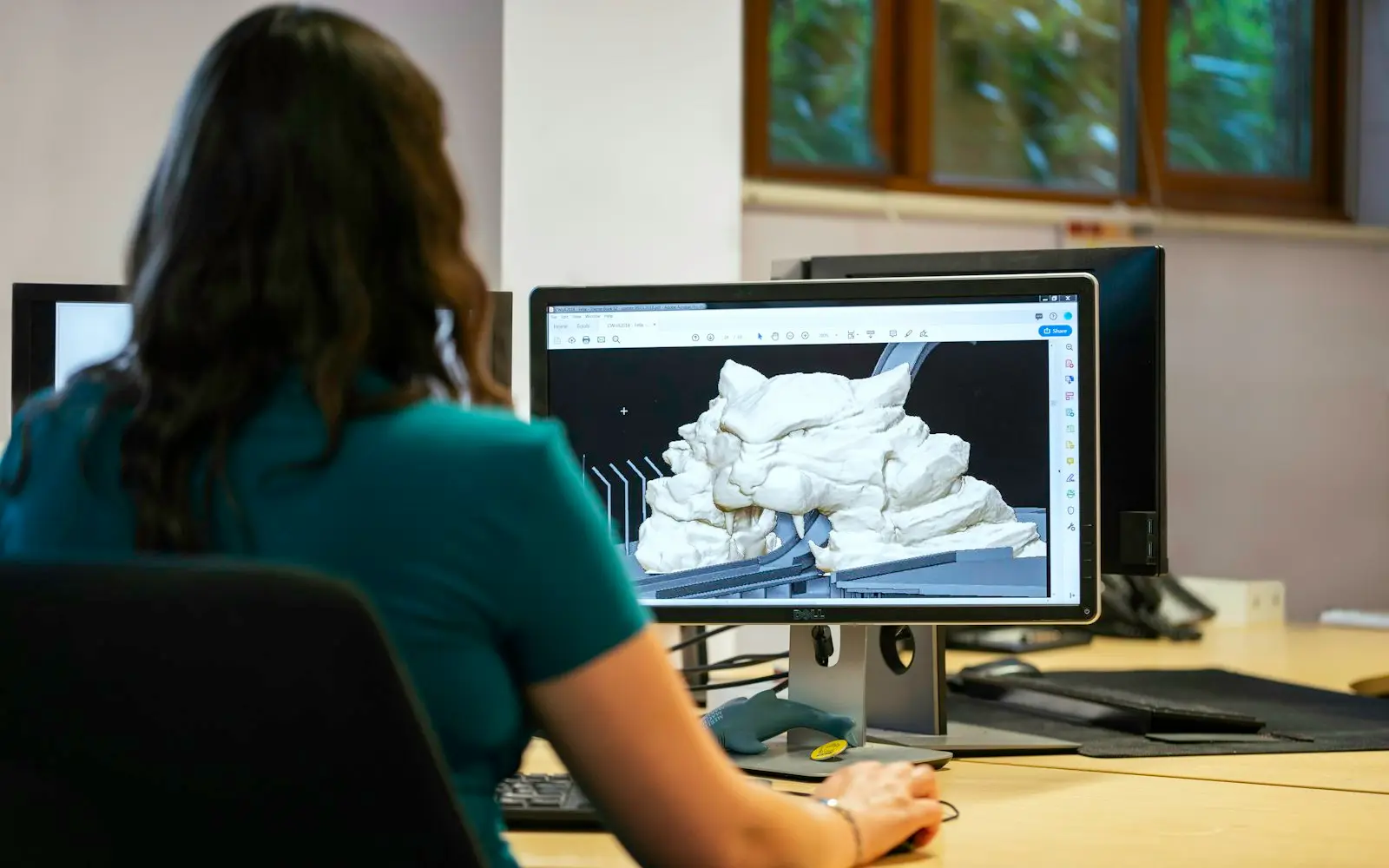 Animator working on a 3D model on a desktop monitor in a daylit studio