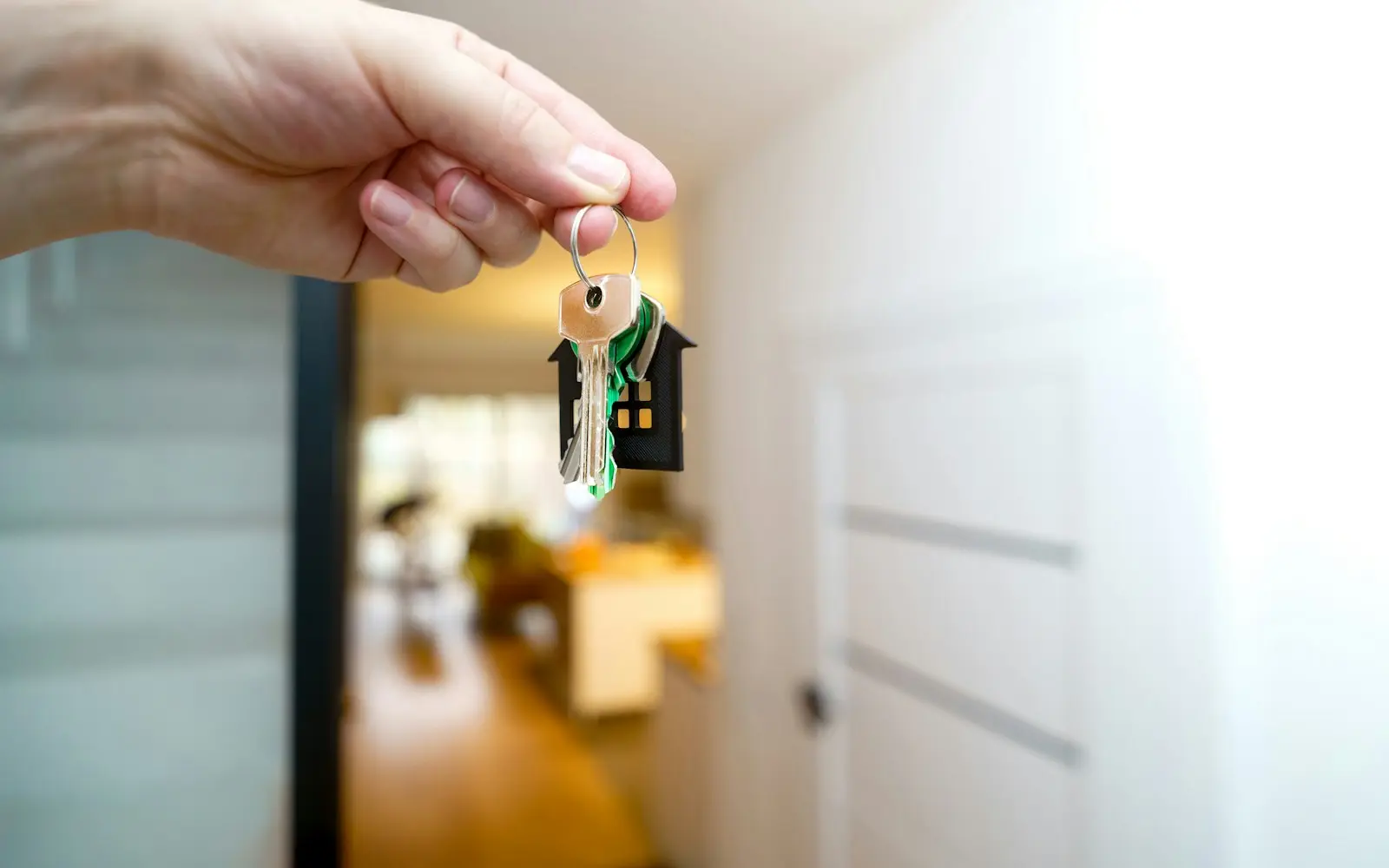 Hand holding house keys with a house-shaped tag in a bright hallway