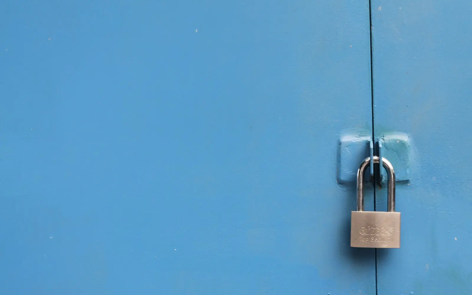 Silver padlock fastened on a blue metal door