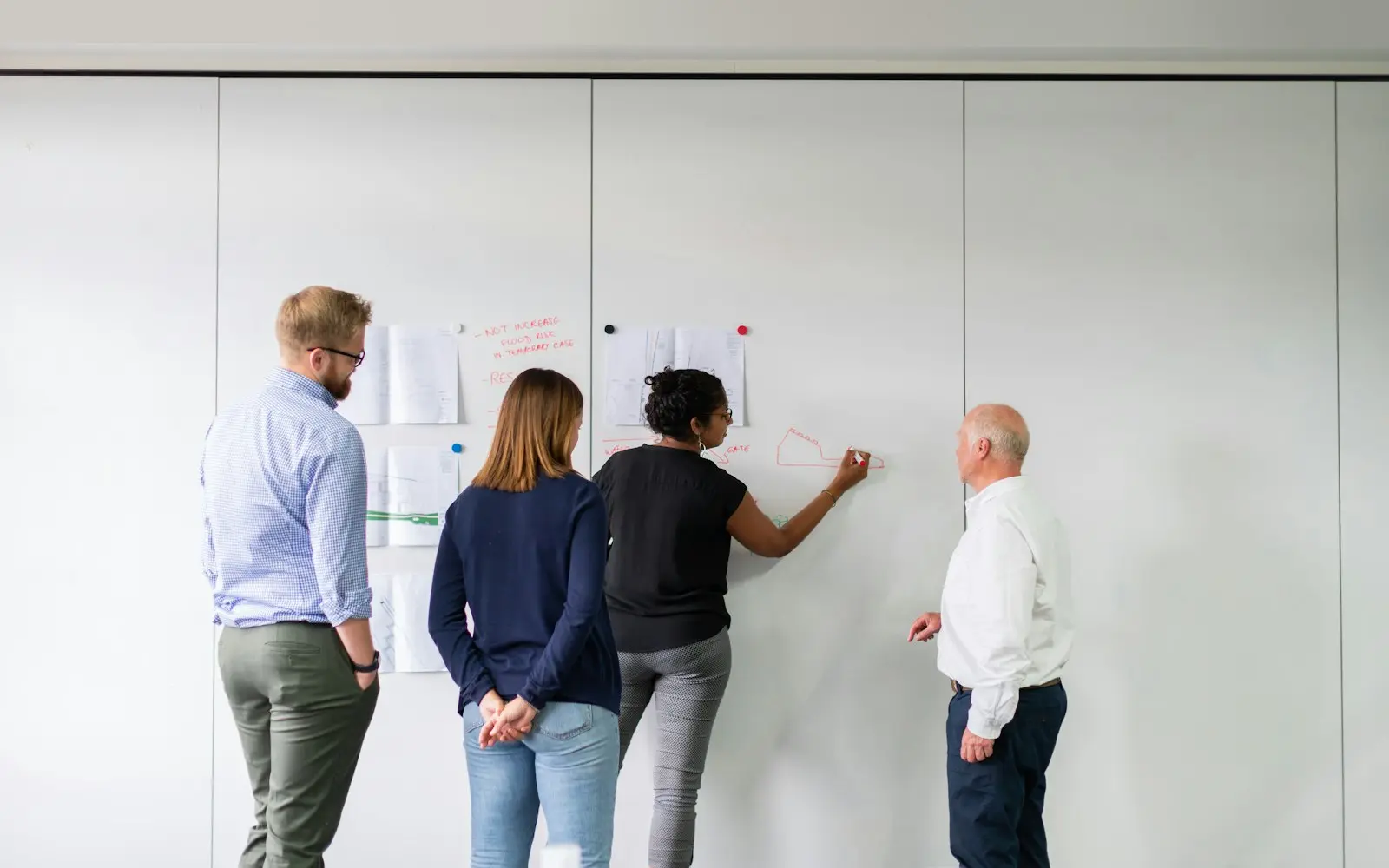 Four colleagues planning together at a wall of pinned notes and sketches